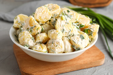 Bowl of tasty Potato Salad with greens on grey background, closeup