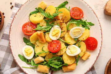 Plate of tasty potato salad with eggs and tomatoes on light background