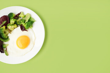 Plate with tasty fried egg, broccoli and spinach on green background