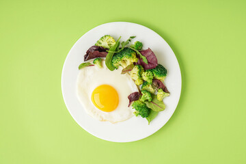 Plate with tasty fried egg, broccoli and spinach on green background