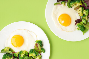 Plates with tasty fried eggs, broccoli and spinach on green background