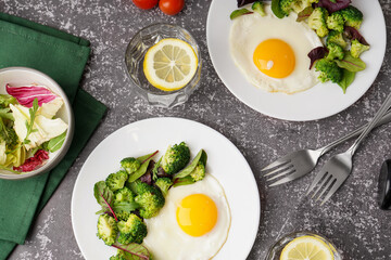 Plates with tasty fried eggs, broccoli and spinach on grey grunge background