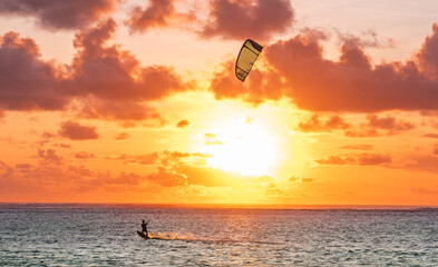 Sunset sky over the Indian Ocean bay with a kiteboarder riding kiteboard with a green bright power...