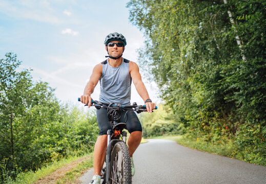 Portrait of happy man dressed in cycling clothes, helmet and sunglasses riding a bicycle on the out-of-town bicycle path. Active sporty people concept image..