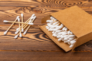 Fototapeta na wymiar Cotton swabs in a craft box on a brown textured wood. Bamboo cotton buds. Means for hygiene of ears. Eco-friendly materials.Hygienic cotton ear buds.