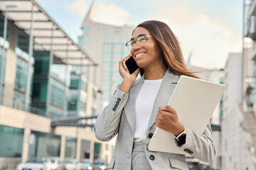 Closeup portrait of successful African American business woman having phone call outdoor. Middle age businesswoman in suit talking on smartphone, walking city urban street at business office center.