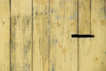Fridged old boards with shabby yellow paint. Part of the old wooden fence in rural areas. A hole for letters