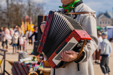 Gentleman musician plays a red accordion at a traditional Baltic cultural event wearing traditional wool  outfit un grey color - obrazy, fototapety, plakaty