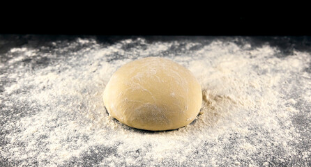 Pizza dough on a dark table sprinkled with flour. Baking concept. Italian cuisine.