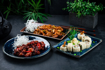 Asian food set of chicken with onion, celery, cashew nuts, pork in Thai sweet chili sauce and sushi roll set with shrimps tempura, cucumber, onion on a dark background.