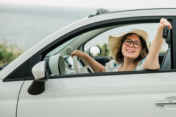 Car driver woman smiling showing new car keys and car. Female driving rented cabrio on summer...