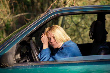 Tired woman driving a car. A middle-aged woman in her forties leaned over the steering wheel of a car. Fatigue, exhaustion, rest during the trip.