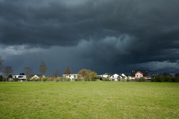 Obraz premium scary natural dark storm clouds in the sky with a housing estate at the straight horizon