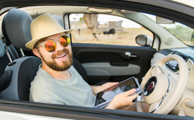 Bearded man using digital tablet inside car while travel and road trip vacation holidays - road map and navigation concept