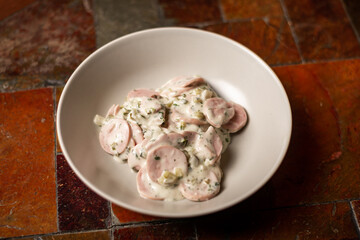Salad of chopped sausages greens and sour cream. Simple meat salad on plate on stone background.