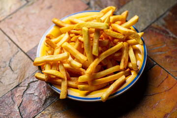Freshly cooked french fries on plate on stone background.