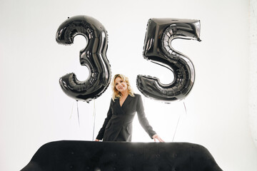 a sexy blonde in a black on background of balloons of numbers thirty-five