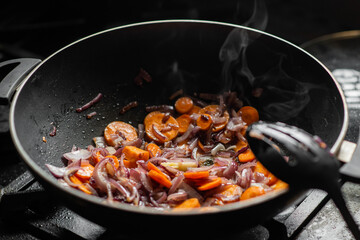Onions and carrots are fried in a deep frying pan. Steam is coming. Preparation for cooking.