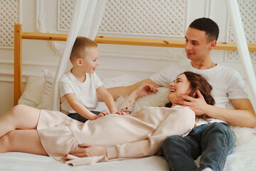 Happy pregnant mom, dad and son play in bed. the concept of family happiness.