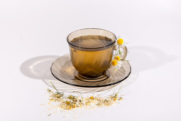Herbal chamomile tea in a transparent cup on a saucer isolated on a white background. A little dry chamomile around the cup. Healthy Eating. Medicinal herb. Used for medicinal purposes.