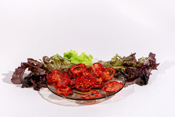 Dried tomato slices on a plate and lettuce leaves isolated on white background. Healthy Eating. Healthy snacks.