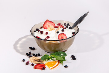 Healthy breakfast. Yogurt with fruit slices and berries in a transparent bowl with a spoon isolated on a white background. Scattered currant berries, mint, dried banana, orange and strawberries slice.
