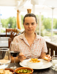 Positive woman eating tomato soup Gazpacho with bread served with glass of wine at restaurant