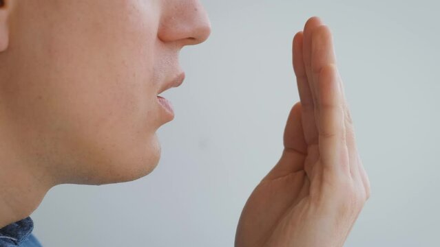 Bad breath. A man breathes into his palm, opening his mouth on white background, close-up