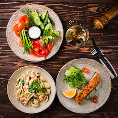 Grilled salmon fillet with cherry tomatoes, lemon and greens with fresh salad and pasta with shrimp.