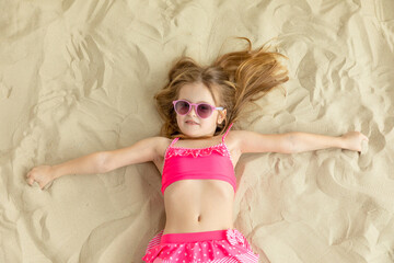 Little girl lying on a sandy beach and sunbathe in the sun