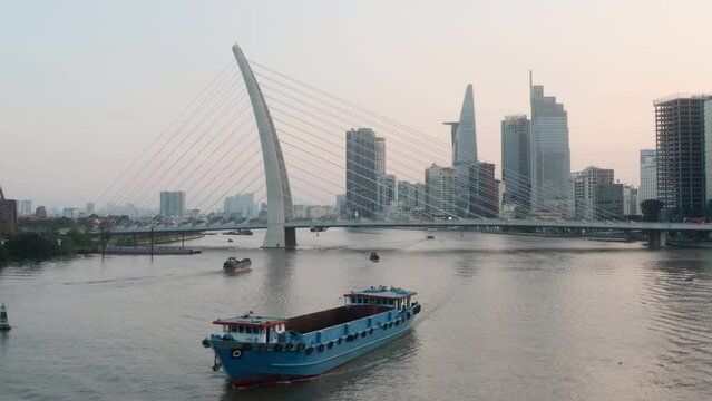 Aerial shot from flying drone of ship floating on the river, cable-stayed bridge and business center with modern skyscrapers in Ho Chi Minh city, early morning time