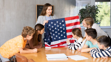 Group of preteen schoolchildren attentively watching teacher describing USA flag in schoolroom
