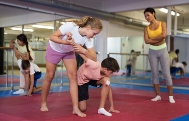 Young boys and girls training self-defence moves during group training. Female trainer standing...