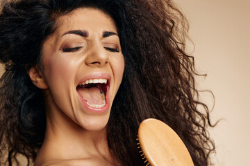 SELF CARE CONCEPT. Concentrated happy joyful awesome curly Latin lady sing in wooden hairbrush like...