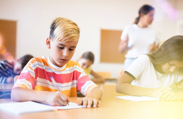 Portrait of diligent schoolboy who writing exercises at lesson in primary school