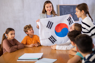 Group of preteen schoolchildren attentively watching pedagogue describing flag of South Korea in schoolroom