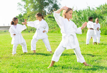 Naklejka na ściany i meble Little girl make karate exercises in summer park