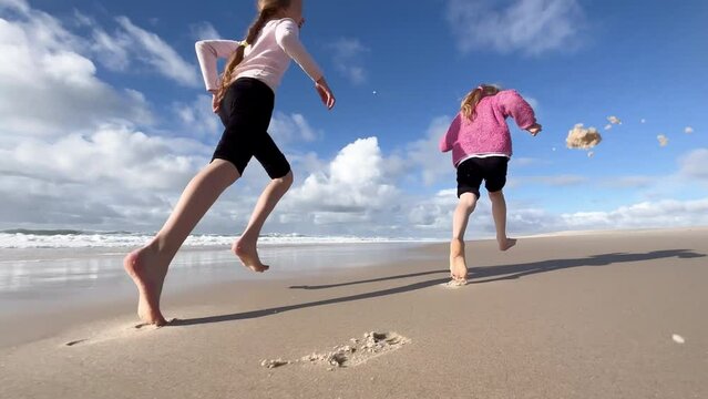 Children run along the coast of the Atlantic Ocean. Two little sisters are playing with the waves on the beach of the Atlantic Ocean. Family time or vacation concept. 4K resolution video.
