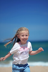 Photo of a little smiling girl running on the beach
