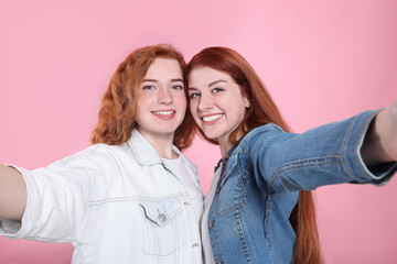Beautiful young redhead sisters taking selfie on pink background