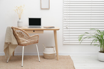 Cozy workspace with modern laptop on desk and comfortable chair at home