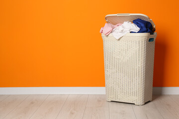 Open laundry basket with clothes near orange wall indoors, space for text