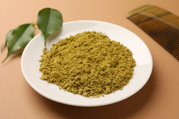 Henna powder, comb and green leaves on coral background. Natural hair coloring