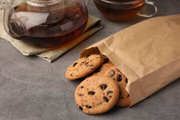 Paper bag with delicious chocolate chip cookies and tea on grey table, closeup. Space for text