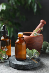 Bottles of eucalyptus essential oil, leaves and mortar on light grey table