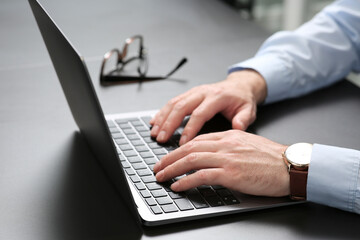 Fototapeta na wymiar Man working on laptop at black desk in office, closeup