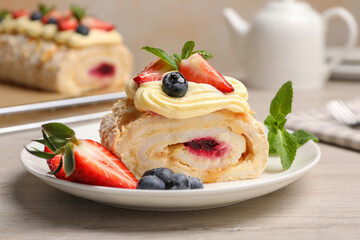 Piece of tasty meringue roll with jam, cream, strawberry, blueberry and mint on white wooden table, closeup