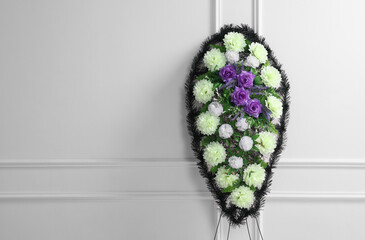 Funeral wreath of plastic flowers near white wall, space for text