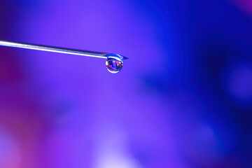 Macro of a liquid drop at the end of a syringe needle, blue background, nobody