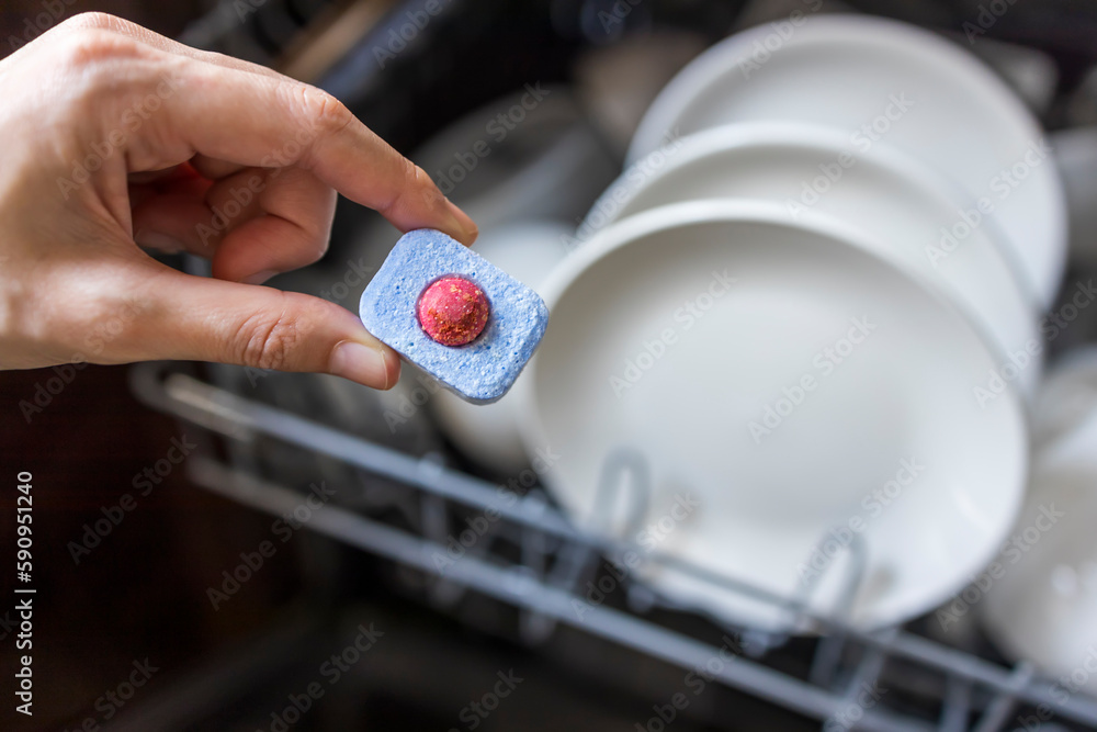 Wall mural close up of woman hand filling dishwasher tablet into open automatic stainless built-in dishwasher m